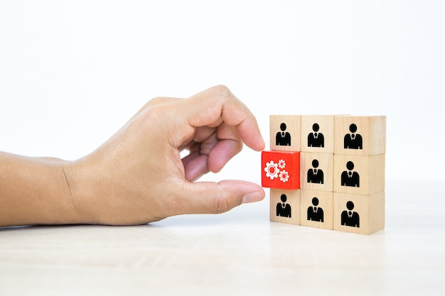 Hand choosing cog icon with people symbol on wooden block stack.