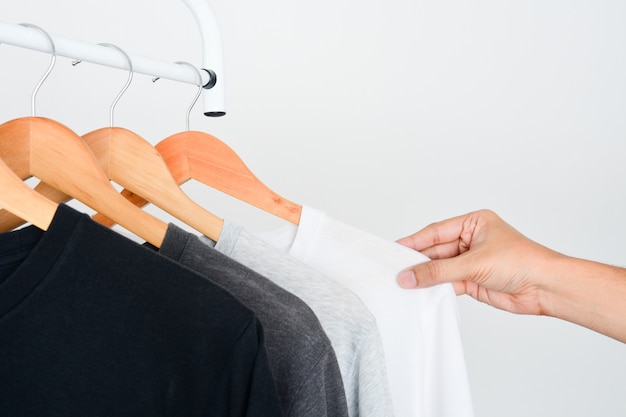 Hand choosing white color tshirt from collection tshirt hanging on a wooden clothes hanger