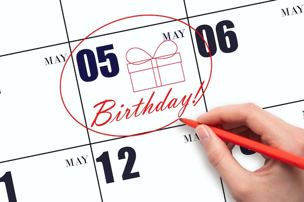 The hand circles the date on the calendar 5 May draws a gift box and writes the text Birthday Holiday