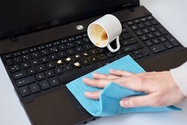 Hand cleans spilled coffee on laptop keyboard with rag