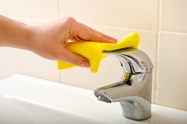 Hand cleans tap with sponge