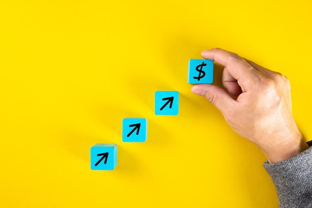 Hand completing conceptual set of business growth on wooden cubes with black arrows and dollar