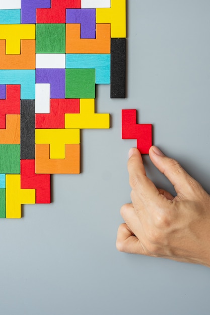 Hand connecting geometric shape block with colorful wood puzzle pieces. 