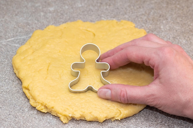 The hand of the cook cutting out the shape of gingerbread men from raw rolled dough on a gray background. The process of making Christmas cookies at home. Christmas food tradition