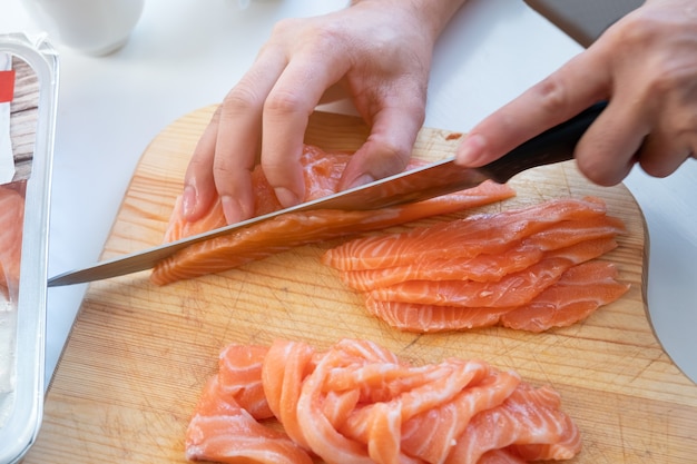 Hand cook using knife slicing a fresh salmon on wooden chopping block