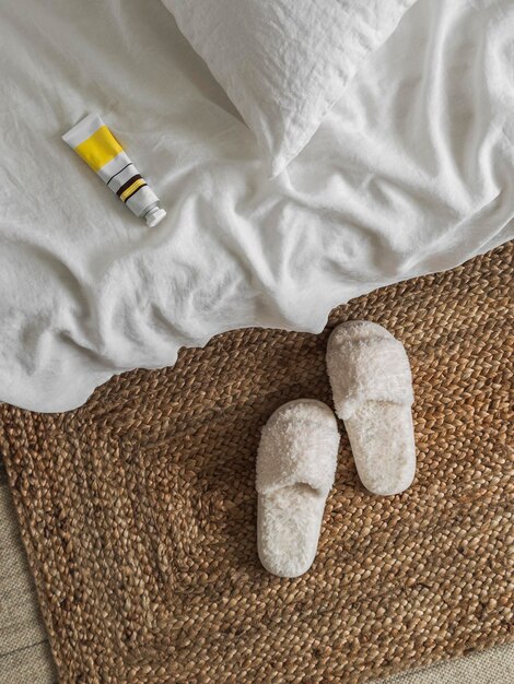 Photo hand cream on the white sheets of the bed slippers cozy home concept