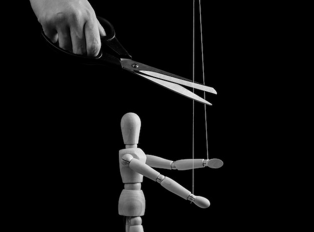 Photo hand cutting strings over puppet with scissors freedom overcoming addiction liberation from slavery abuse abusive toxic relationship cessation concept black and white