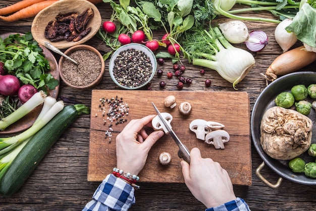 Verdure di taglio a mano. le mani delle donne stanno affettando i funghi sulla tavola di legno vicino alle verdure.