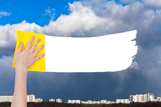 Hand deletes rainy clouds over city by yellow rag