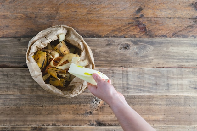 Hand deponeren van fruitresten in een papieren zak met composteerbare fruitschillen.