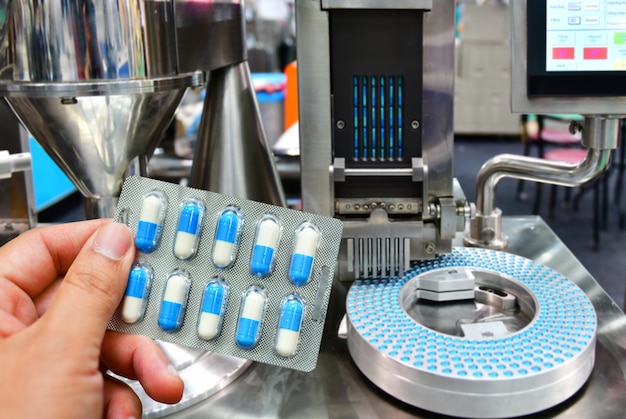 Hand die blauw capsulepak houden bij de productielijn van de geneeskundepil, Industrieel farmaceutisch concept.