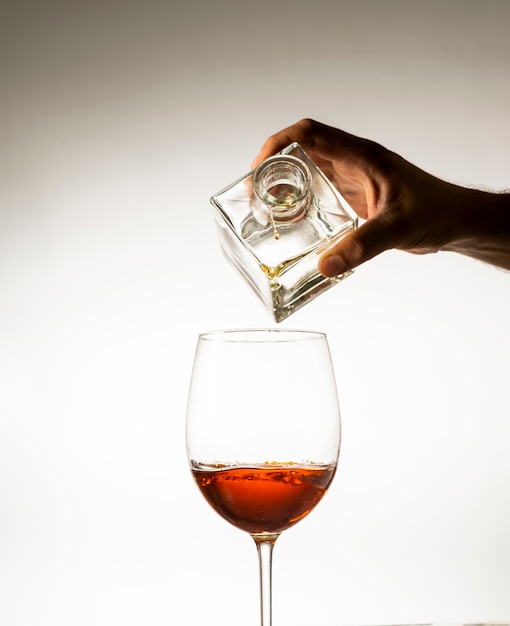 Hand die cognac giet in een glas op een lichte achtergrond