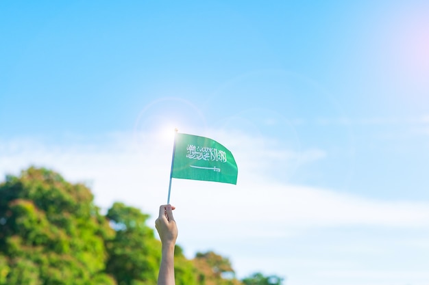 Hand die de vlag van Saudi-Arabië op blauwe hemelachtergrond houdt. Nationale dag van september Saoedi-Arabië en gelukkige vieringsconcepten