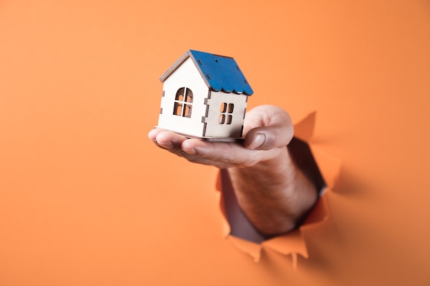 Hand die een huisminiatuur op oranje achtergrond houdt