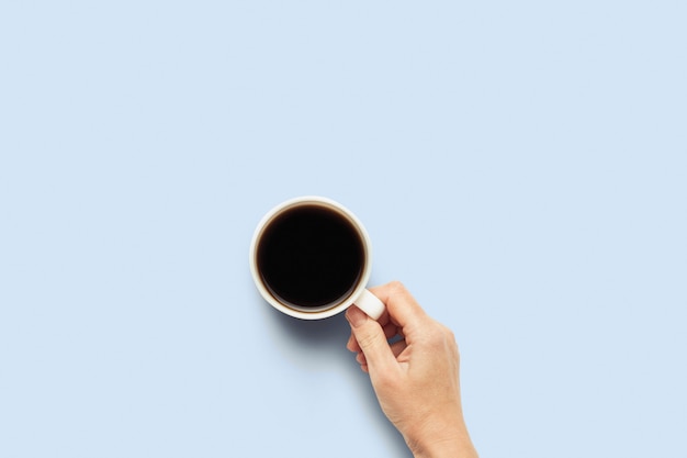 Hand die een kop met hete koffie op een blauwe achtergrond houdt. Ontbijtconcept met koffie of thee. Goedemorgen, nacht, slapeloosheid. Plat lag, bovenaanzicht