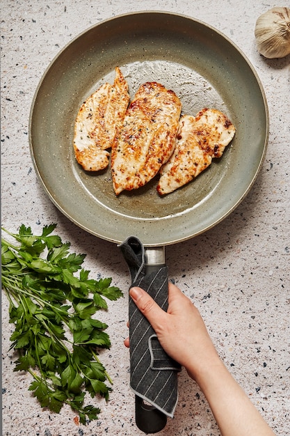 Hand die een pan houdt die gemarineerde kippenborstfilets kookt