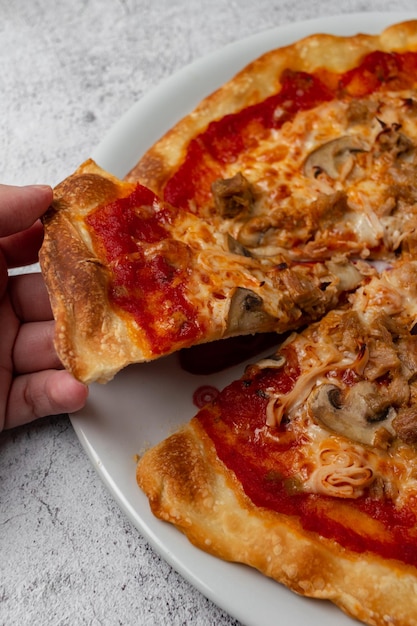 Hand die een plak pizza met tomatenkaas, champignons, tonijngroenten en ham neemt