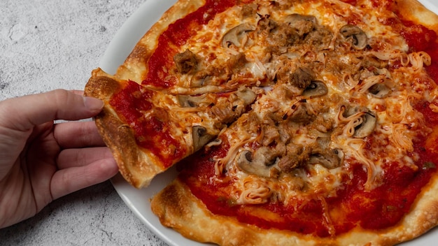 Hand die een plak pizza met tomatenkaas, champignons, tonijngroenten en ham neemt