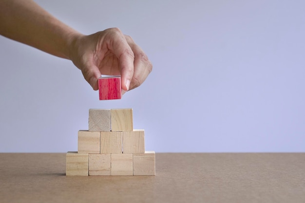 Hand die een rood houtblok op een stapel piramidehoutblokken zet