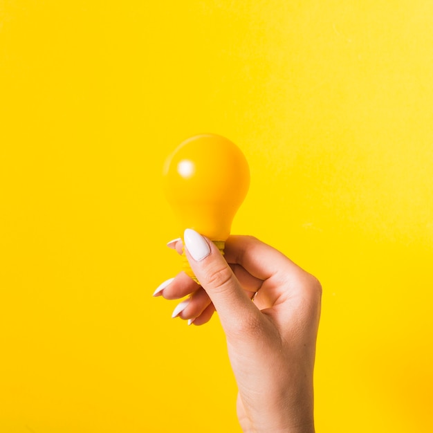 Foto hand die gele gloeilamp houdt tegen gekleurde achtergrond