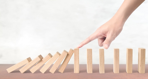 Hand die het Domino-effect op houten blokken tegenhoudt