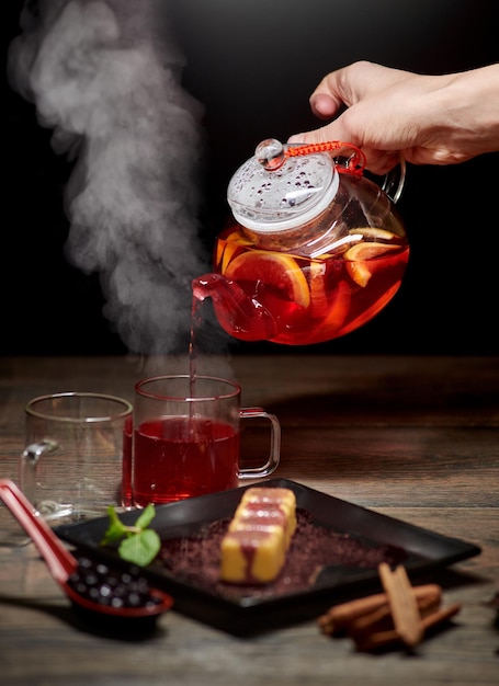 Hand die hete thee uit glazen waterkoker giet Stomende thee in glazen Heerlijk Japans zoet dessert op donkere achtergrond
