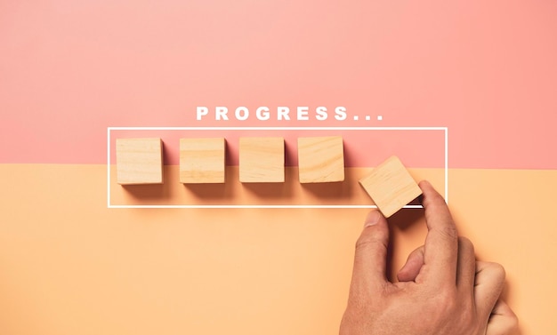 Foto hand die houten kubusblok op de helft van roze en oranje achtergrond zet met grafisch laden voor progressief projectconcept.