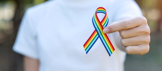 Hand die LGBTQ-Regenbooglint toont tegen hemelachtergrond in de ochtend.