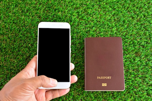 Foto hand die mobiele telefoon, paspoort op groen gras houdt. kan worden gebruikt voor zaken en reizen