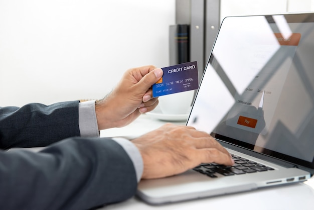 Hand die van de creditcard van de zakenmanholding betaling online met laptop computer verrichten