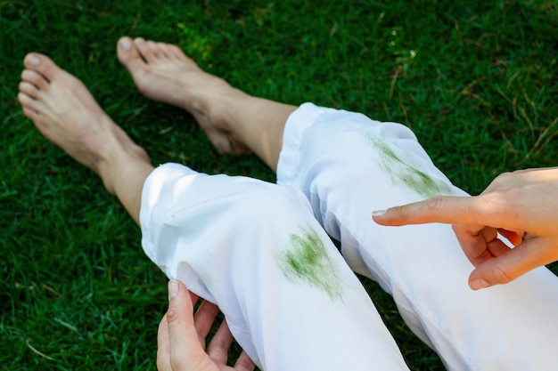 Hand die vuile vlek van gras op witte broek toont van onverwacht ongeval bovenaanzicht