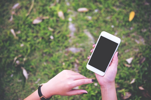 Hand die witte mobiele telefoon met het lege zwarte scherm op de groene achtergrond van de tuinaanbod houden