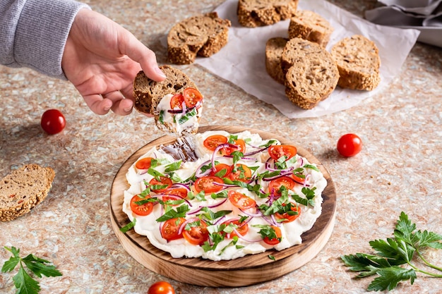 Hand dipping bread into a buttered board with tomatoes onions and herbs