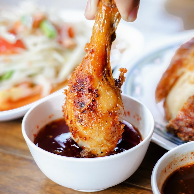 A hand dipping a chicken leg into a bowl of sauce