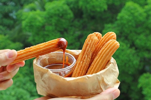 Hand Dipping a Stick of Fresh Fried Churro in Dolce de Leche or Caramel Sauce