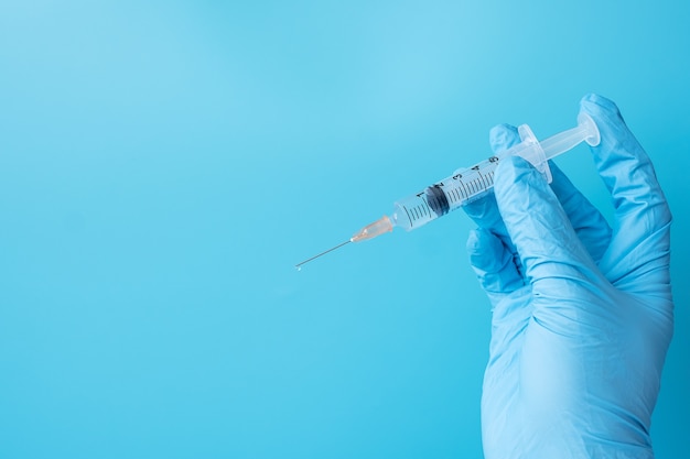 Hand of doctor injection vaccine or drug by Needle Syringe on blue background.