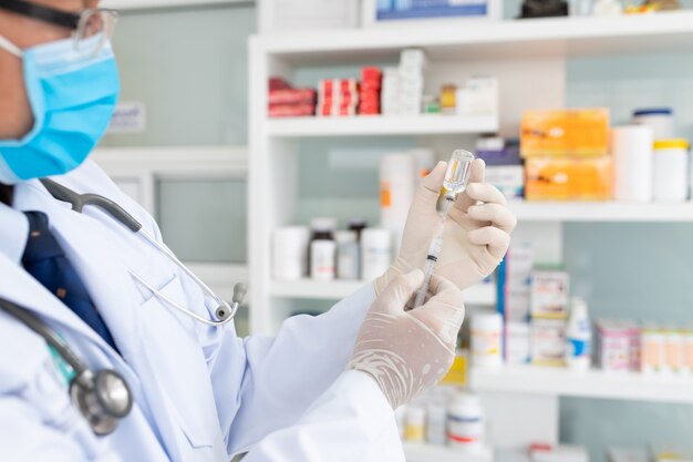 hand of doctor or nurse holding syringe and vaccine.researcher hand in gloves holding flu, coronavirus vaccine disease preparing for human clinical trials vaccination shot, medicine and drug.