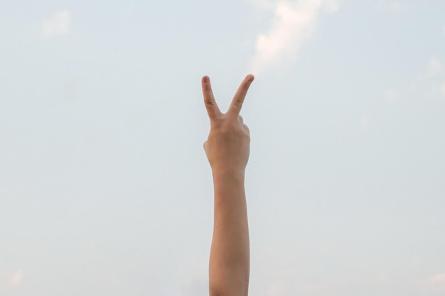 Рука, показывающая номер два, жест символа на ярко-голубом летнем небе на фоне природы, жестикуляция номер два, номер два на языке жестов, второй и подсчет двух понятий, два пальца вверх.