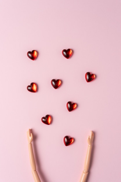 Hand of a doll with small hearts on a pink surface.