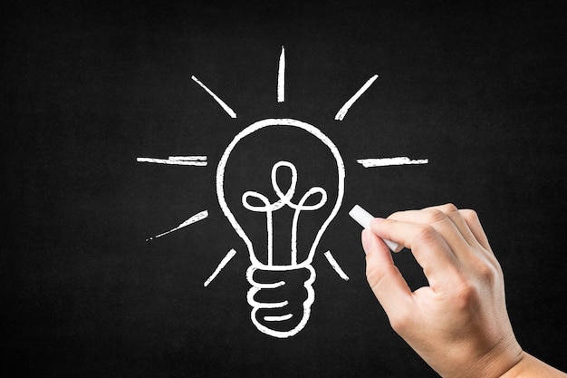 Photo hand drawing a light bulb on a blackboard