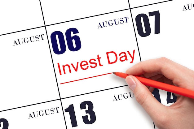 Рука рисует красную линию и пишет текст Invest Day на календарную дату 6 августа Бизнес и финансовая концепция