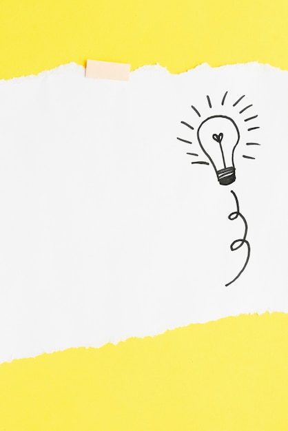 Hand drawn light bulb on white card paper over yellow backdrop