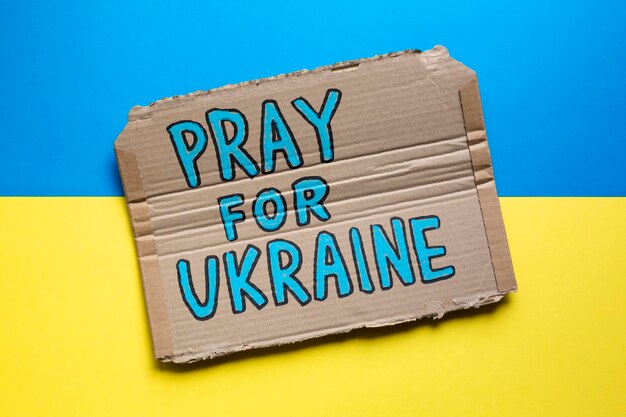 Hand drawn sign with Pray For Ukraine slogan on Ukrainian flag