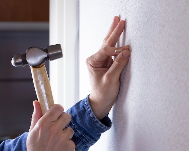 Hand driving a nail into the wall with a hammer