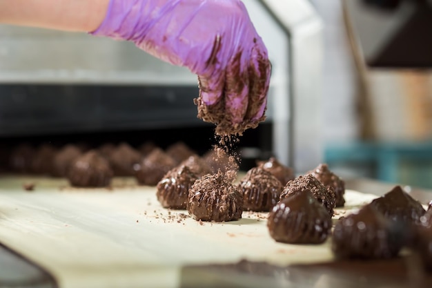 お菓子に削りくずを手で落とします。キャンディーと手袋をはめます。労働者の最後の仕上げ。チョコレートの余分なグラムはほとんどありません。