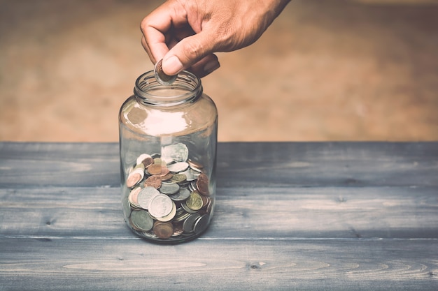 hand drops money into a glass jar for a savings