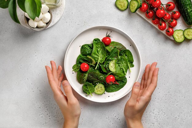 Hand en groene salade bladeren met rucola spinazie komkommer tomaten op grijze achtergrond Top view