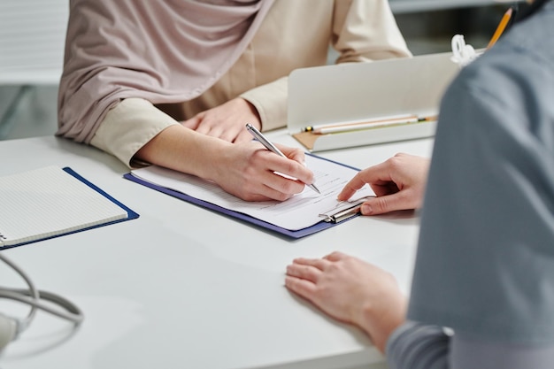 Hand of female clinician pointing at medical document while patient signing it