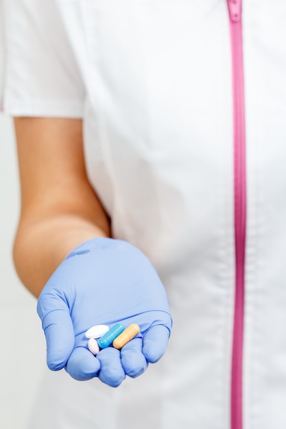 Рука женщины-врача в синей перчатке с кучей таблеток разного цвета с акцентом на таблетки