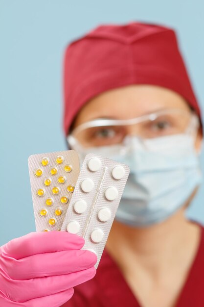 Hand of female doctor in pink latex glove holding blisters with pills Selective focus on pills